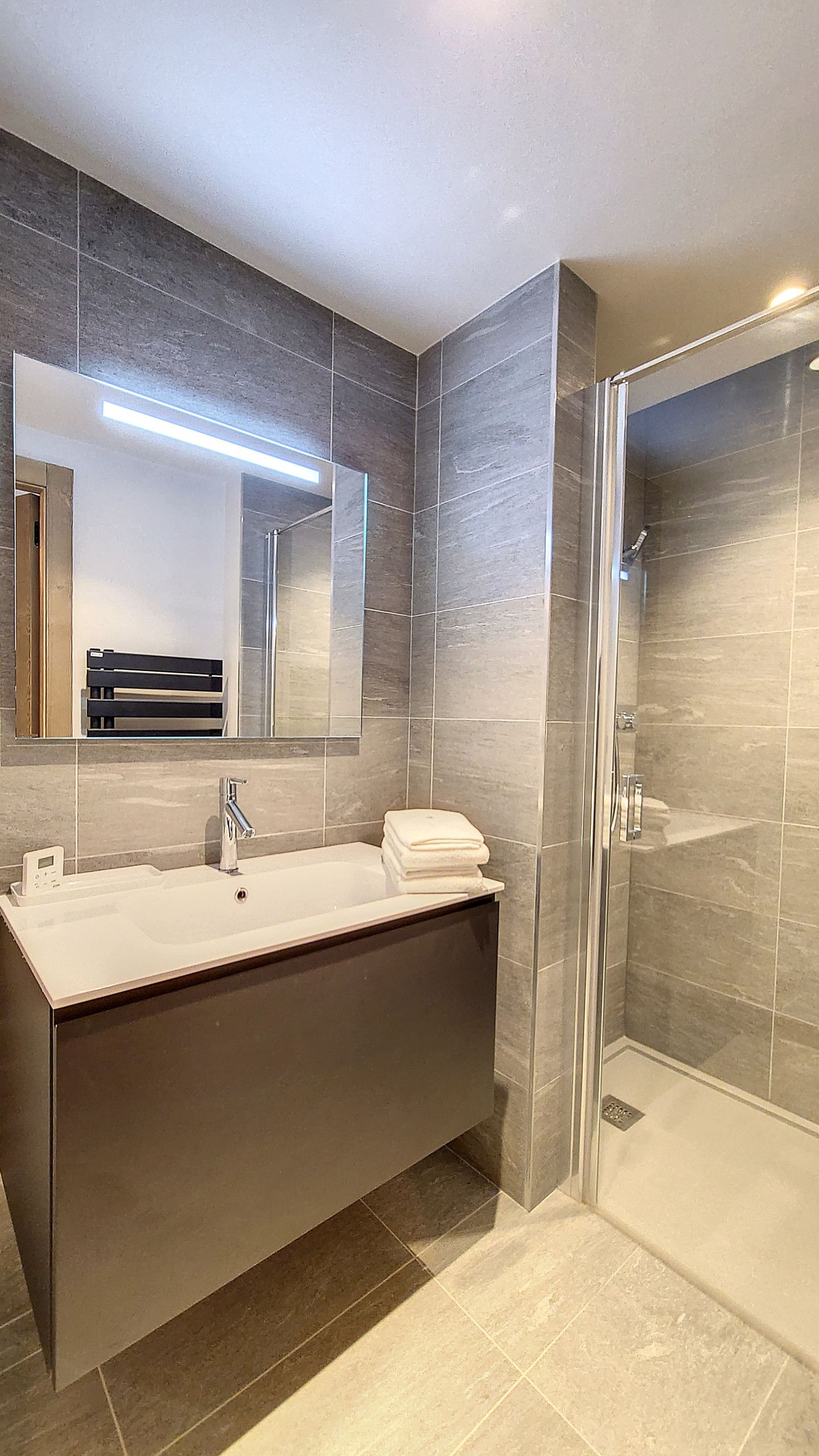 A modern bathroom with a large mirror, a dark-colored vanity, a glass shower enclosure, and a white sink.
