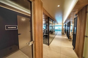 A hallway with a door labeled 'HAMMAM' leading to a fitness area with exercise equipment.