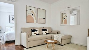 Una sala de estar moderna con un sofá color beige, una mesa redonda de madera y un espejo grande.
