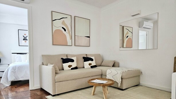 Una sala de estar moderna con un sofá color beige, una mesa redonda de madera y un espejo grande.