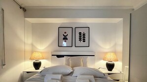 Una cama bien hecha con dos almohadas y dos toallas enrolladas, dos lámparas de noche y dos cuadros en la pared.