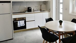 Una cocina moderna con armarios blancos, salpicadero de mármol, horno empotrado y zona de comedor con mesa y sillas redondas.