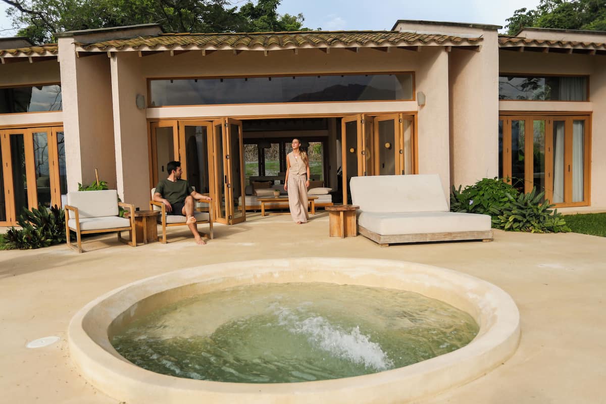 A modern house with a large outdoor pool, wooden furniture, and a spacious patio area.