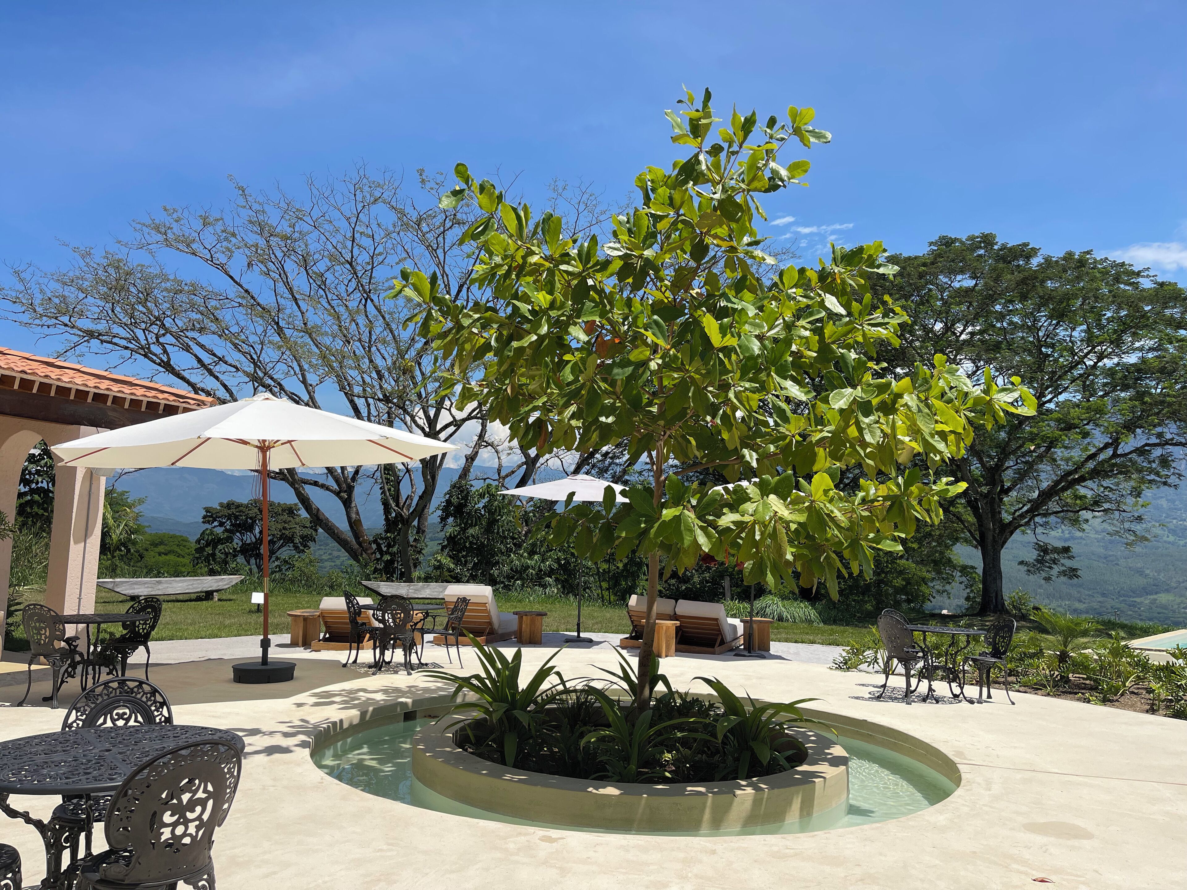 An outdoor patio with a pool, surrounded by lounge chairs and umbrellas, overlooking a scenic landscape.