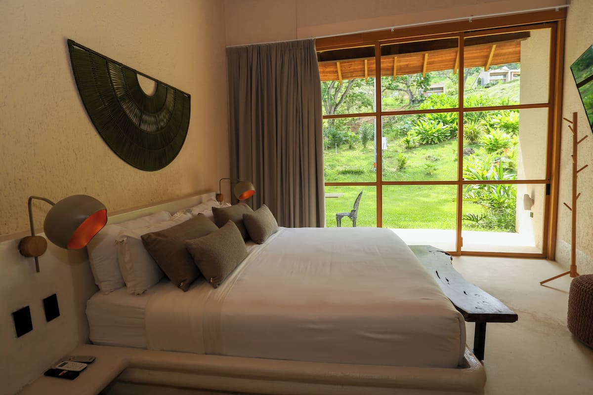 A bedroom with a large bed, a view of a garden, and a wooden bench.