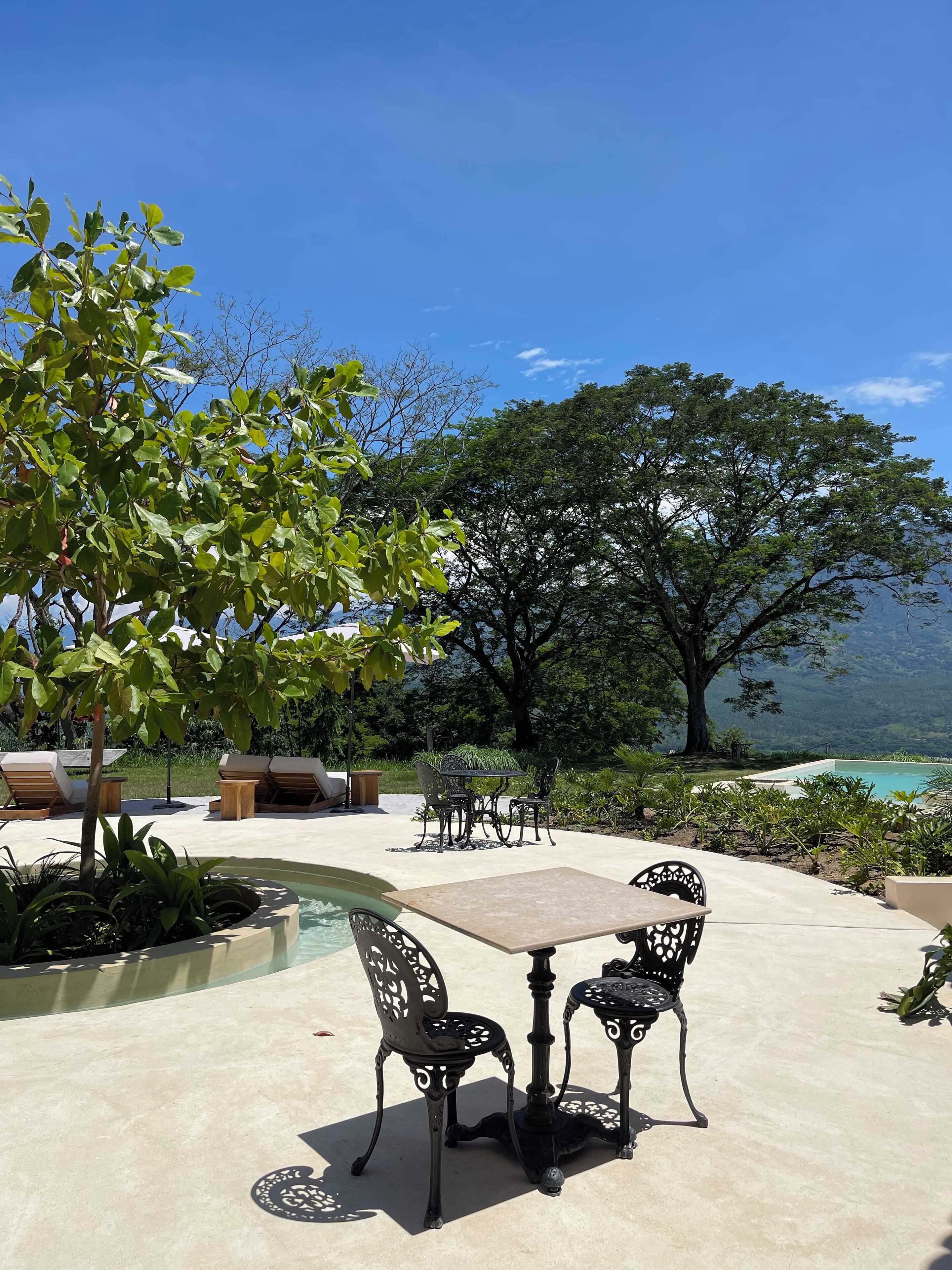 Un patio exterior con piscina, sillones de descanso y una mesa con sillas.