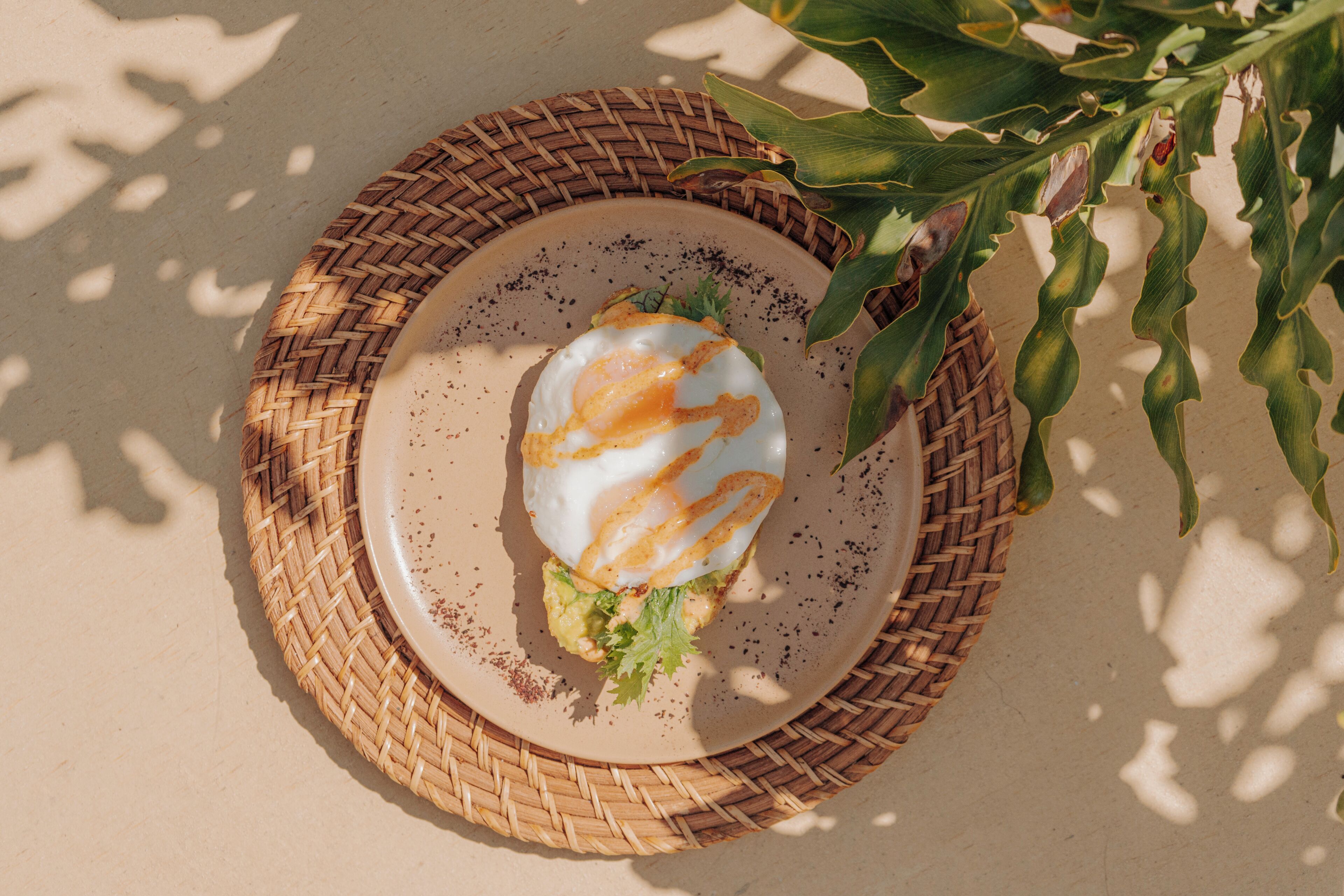 A plate with a fried egg and avocado on a woven mat.