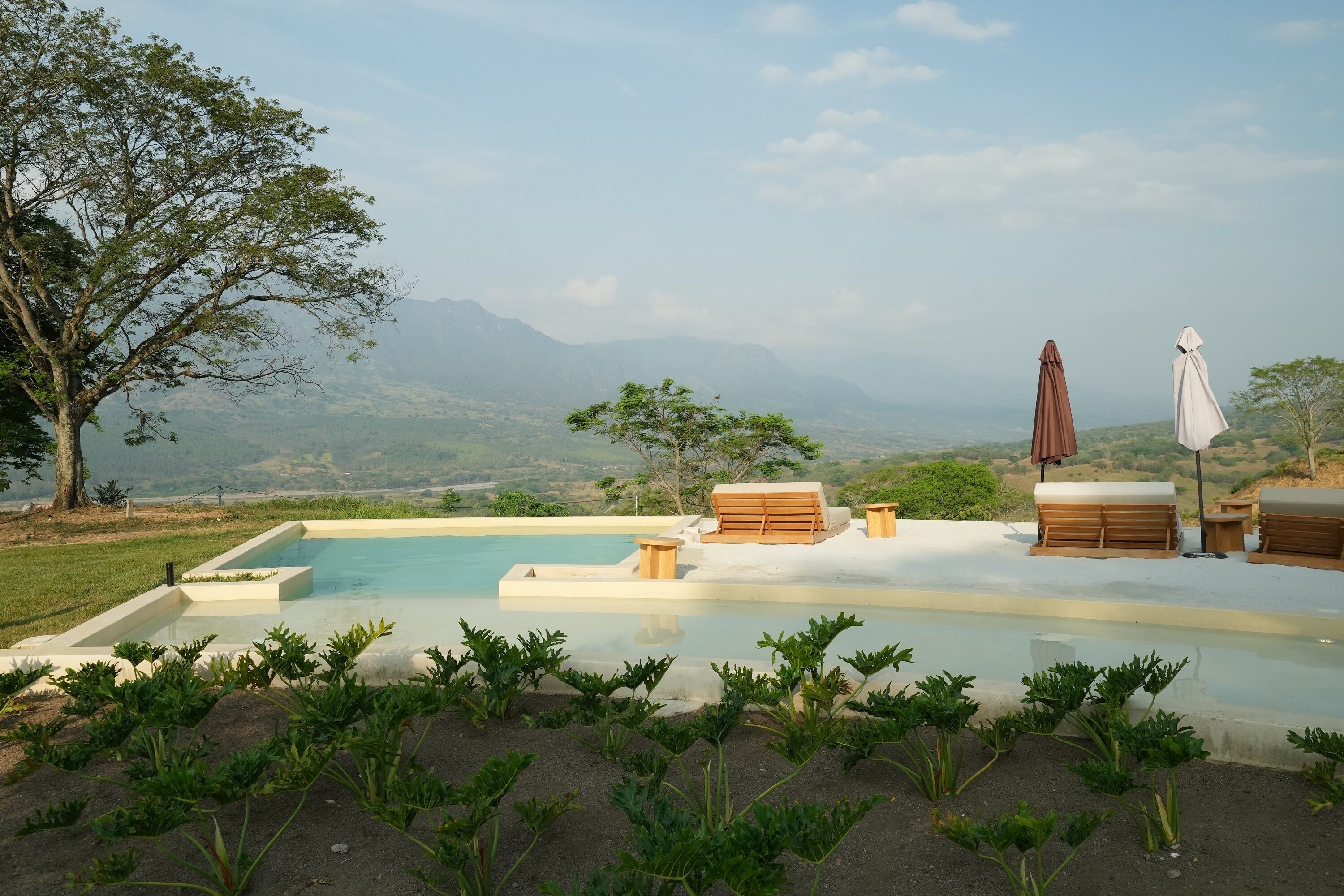 Una piscina infinita con tumbonas de madera y vistas a montañas distantes.