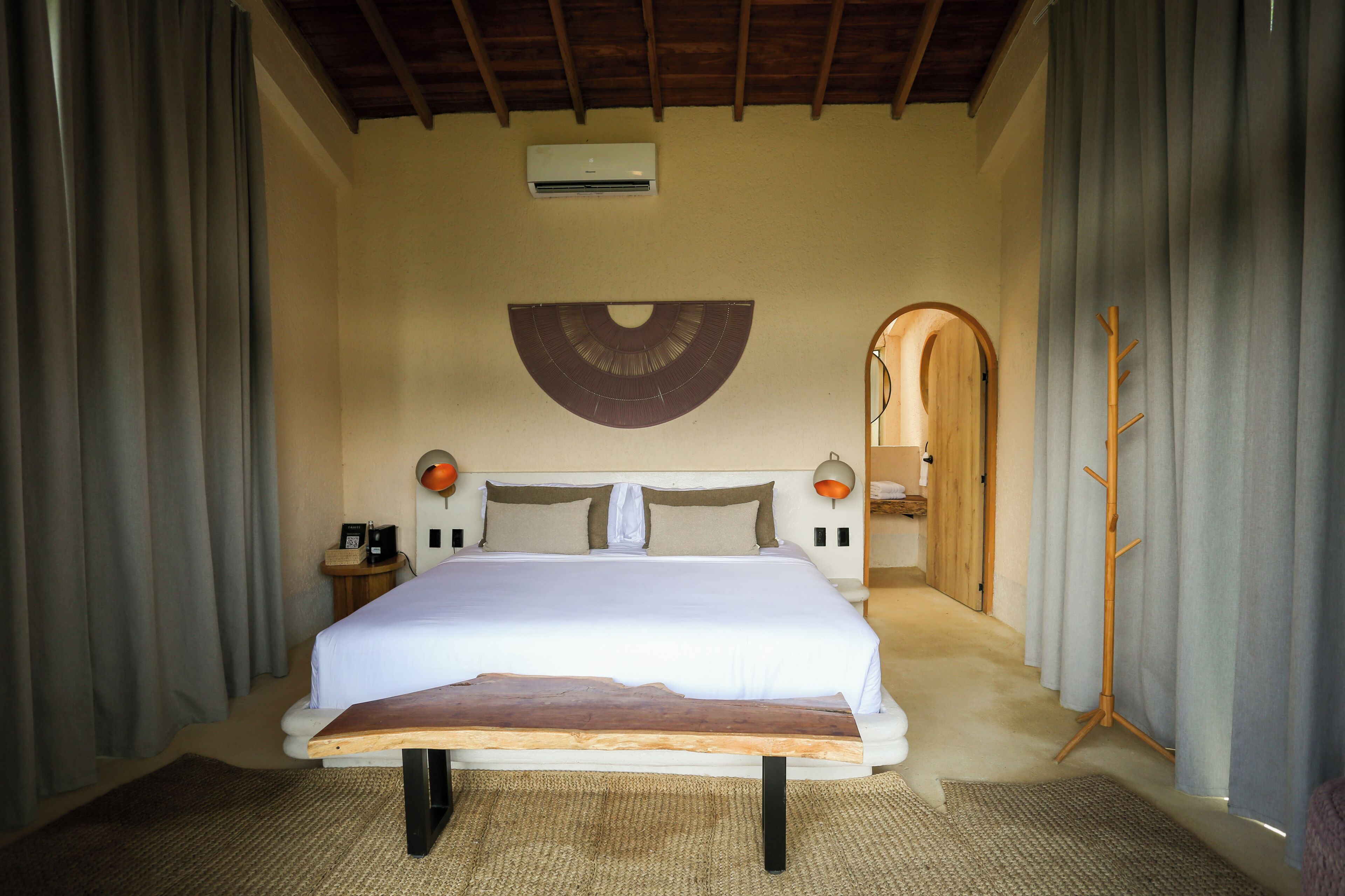 A bedroom with a large bed, a wooden headboard, a wall-mounted fan, and a wooden coat rack.