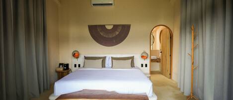 A bedroom with a large bed, a wooden headboard, a wall-mounted fan, and a wooden coat rack.