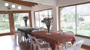 A dining area with a long table, white chairs, and a wooden ceiling. - Quinta San Martin (Ollantaytambo)