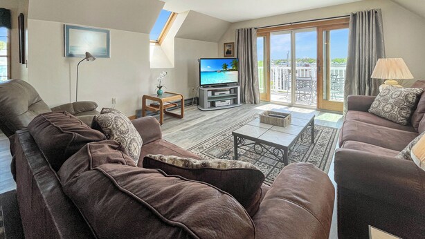 A living room with a flat-screen TV, two sofas, a coffee table, and a balcony with a view. - High View at Short Sands - Beautiful condo at Short Sands Beach (York)