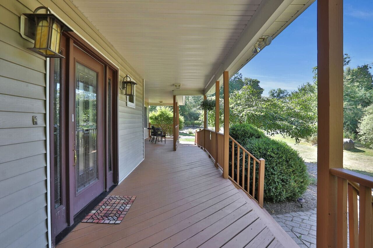 A covered porch with a wooden railing, a door with glass panels, and a small table with chairs.