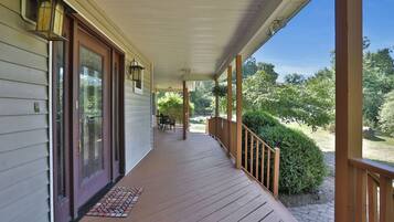 A covered porch with a wooden railing, a door with glass panels, and a small table with chairs.