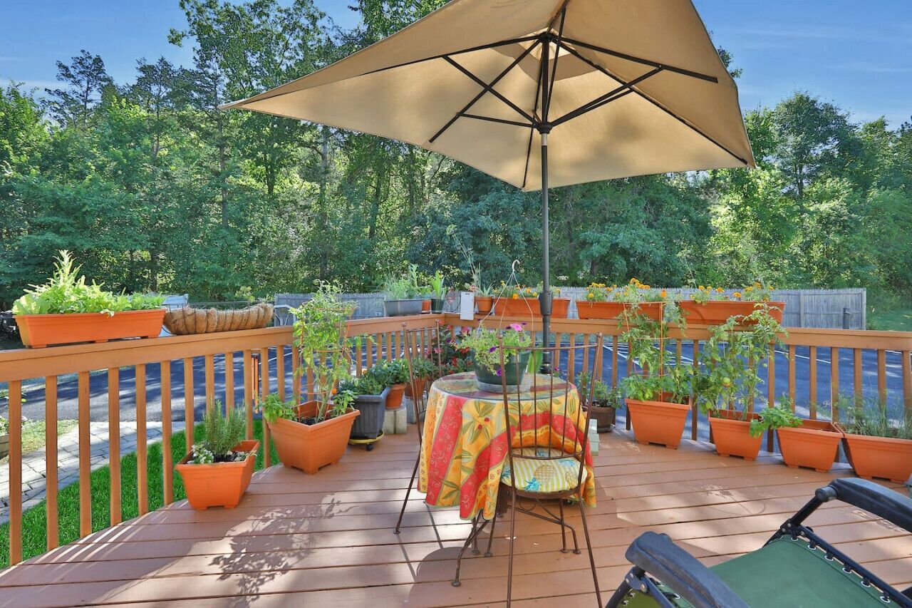 Una terraza con mesa y sillas, rodeada de plantas en macetas y una valla de madera.