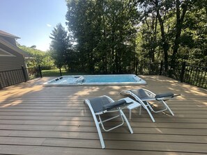 A wooden deck with a hot tub and two lounge chairs.
