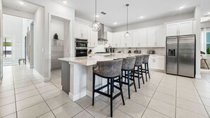 A modern kitchen with white cabinets, a stainless steel refrigerator, and a central island with bar stools. - 5BR, Reunion Resort, villa, games room (Kissimmee)