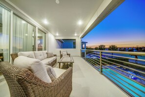 Un balcone con mobili in vimini, una piscina e vista sulla città al crepuscolo.