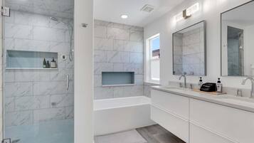 Une salle de bain moderne dotée d’une douche à l’italienne, d’une baignoire et d’un meuble-lavabo double avec des miroirs.