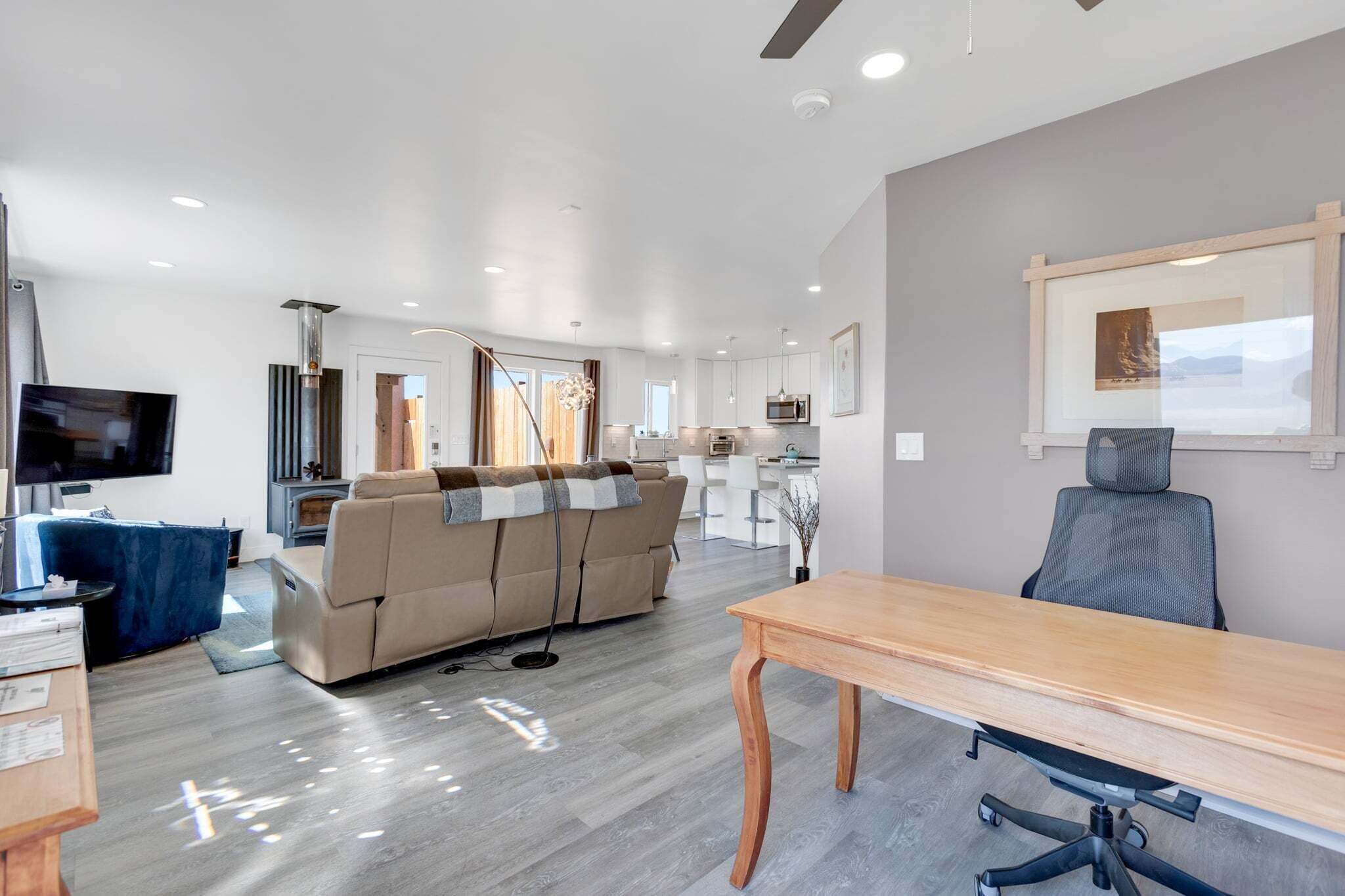 A modern living room with a sofa, a TV, a dining table, and a kitchen in the background.