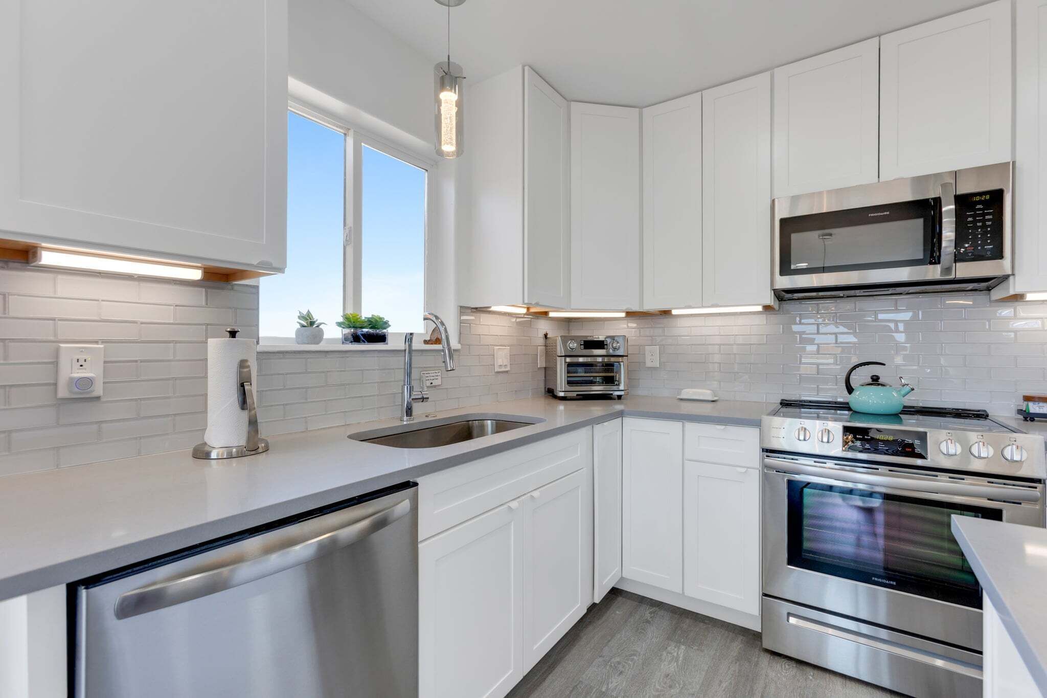 A modern kitchen with white cabinets, stainless steel appliances, and a window providing natural light.