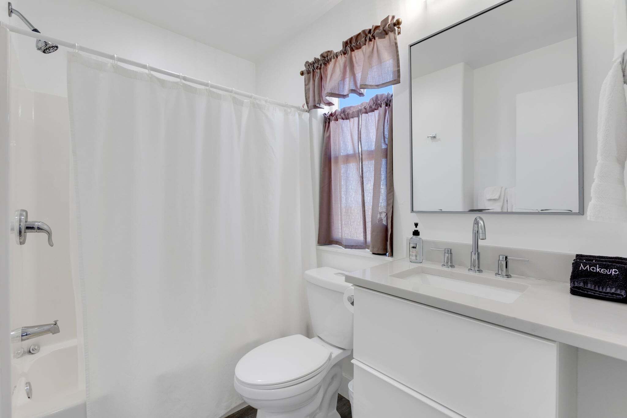 A bathroom with a shower curtain, a toilet, a sink with a mirror, and a makeup bag on the counter.