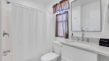 A bathroom with a shower curtain, a toilet, a sink with a mirror, and a makeup bag on the counter.