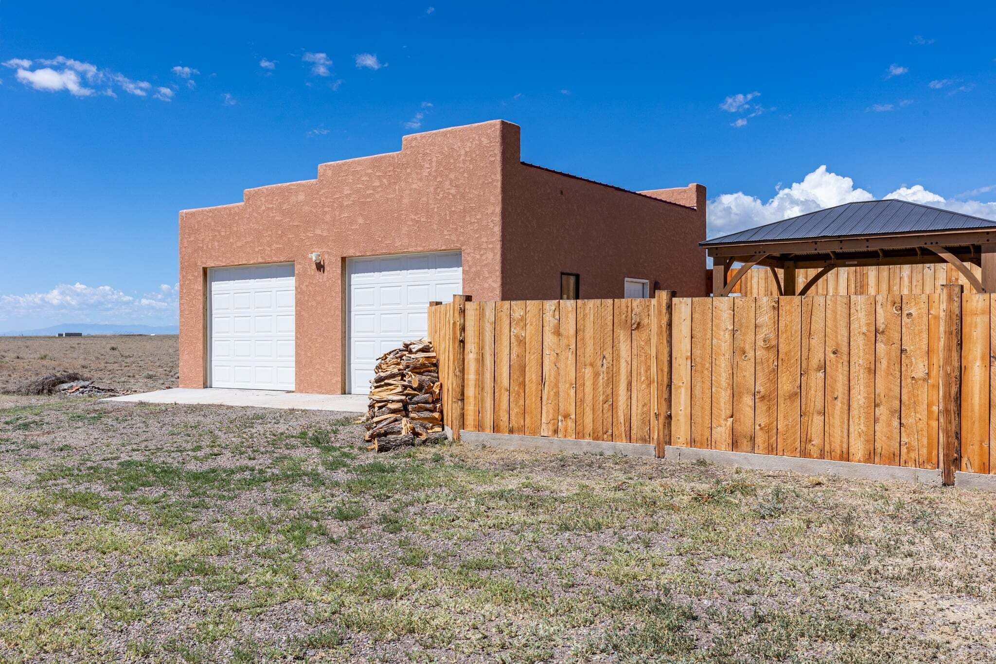 A single-story building with a garage, a wooden fence, and a stack of firewood.