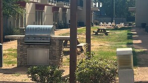 Un patio al aire libre con una parrilla, una mesa de picnic y una estructura de pérgola.