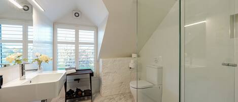Un baño moderno con cabina de ducha de vidrio, un lavamanos blanco y un ventanal con persianas.