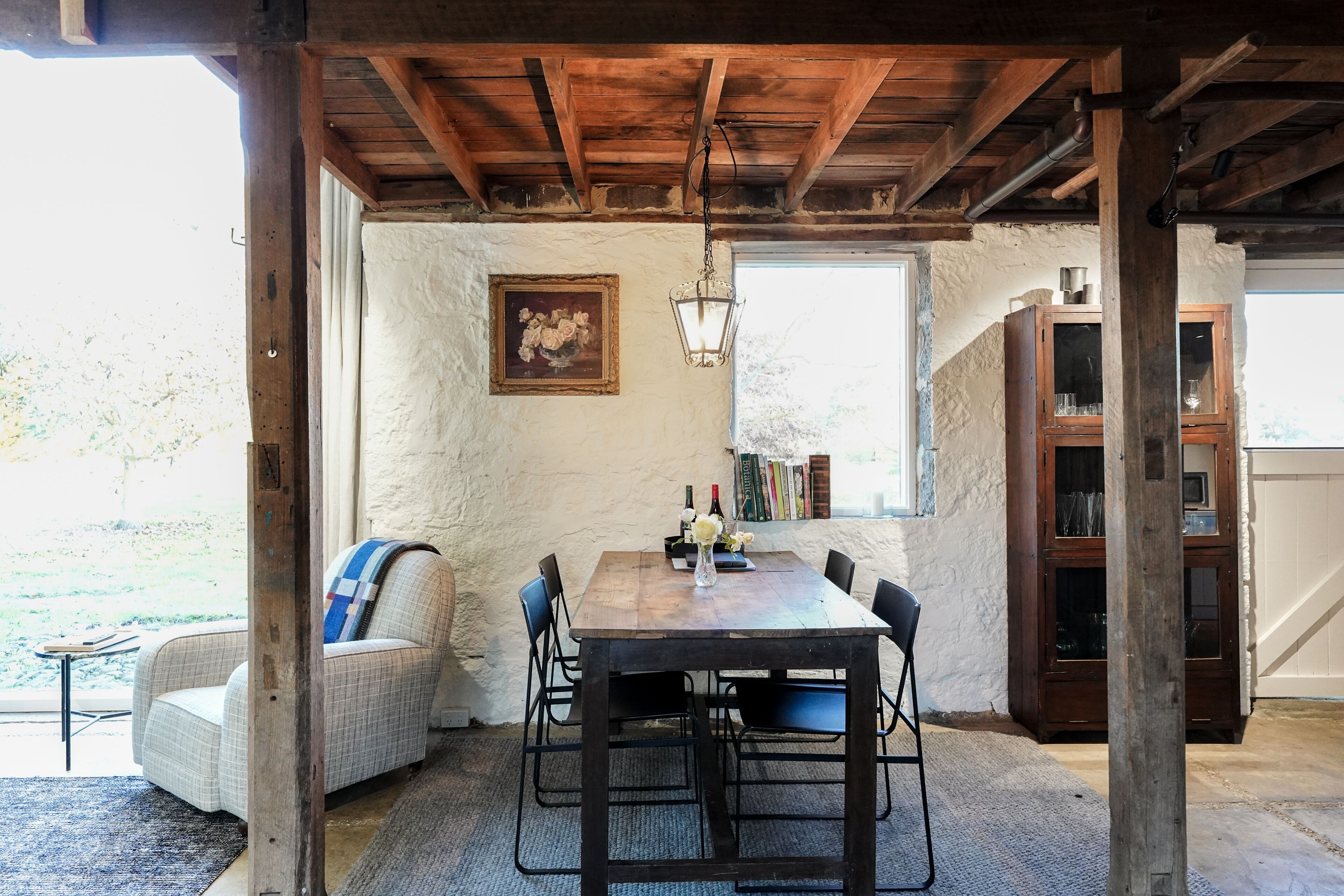 Un comedor rústico con una mesa de madera, sillas y un banco. Se ve un cuadro y un aparador al fondo.
