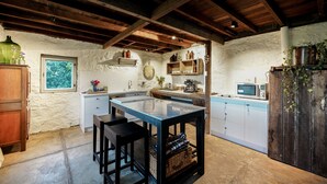 A rustic kitchen with a central island, wooden stools, and a stone floor. - Honeysuckle Barn & Garden (Kyneton)