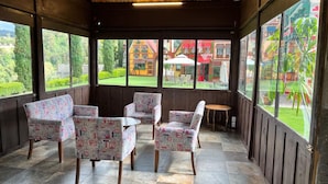A covered outdoor seating area with patterned chairs and a small table, overlooking a well-maintained garden and colorful buildings. - Villa Clauss (Tlalpujahua)