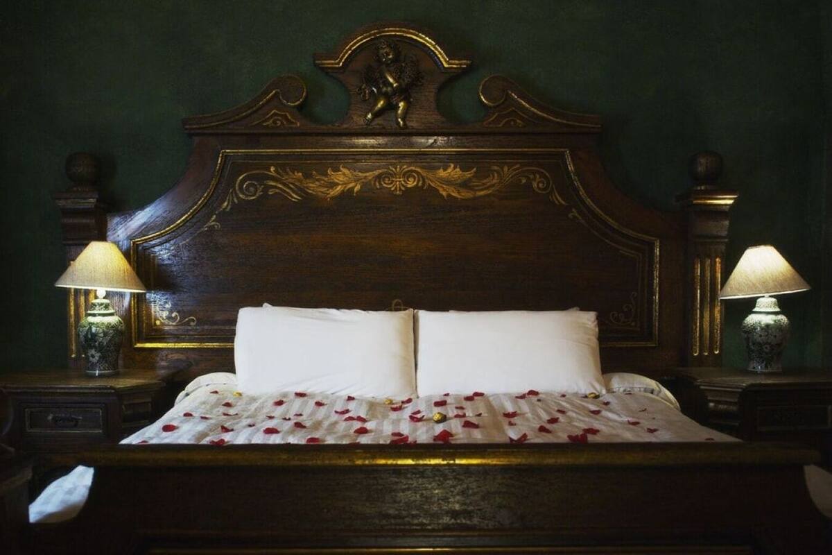 A bed with a wooden headboard, two bedside lamps, and a bedspread with red rose petals.