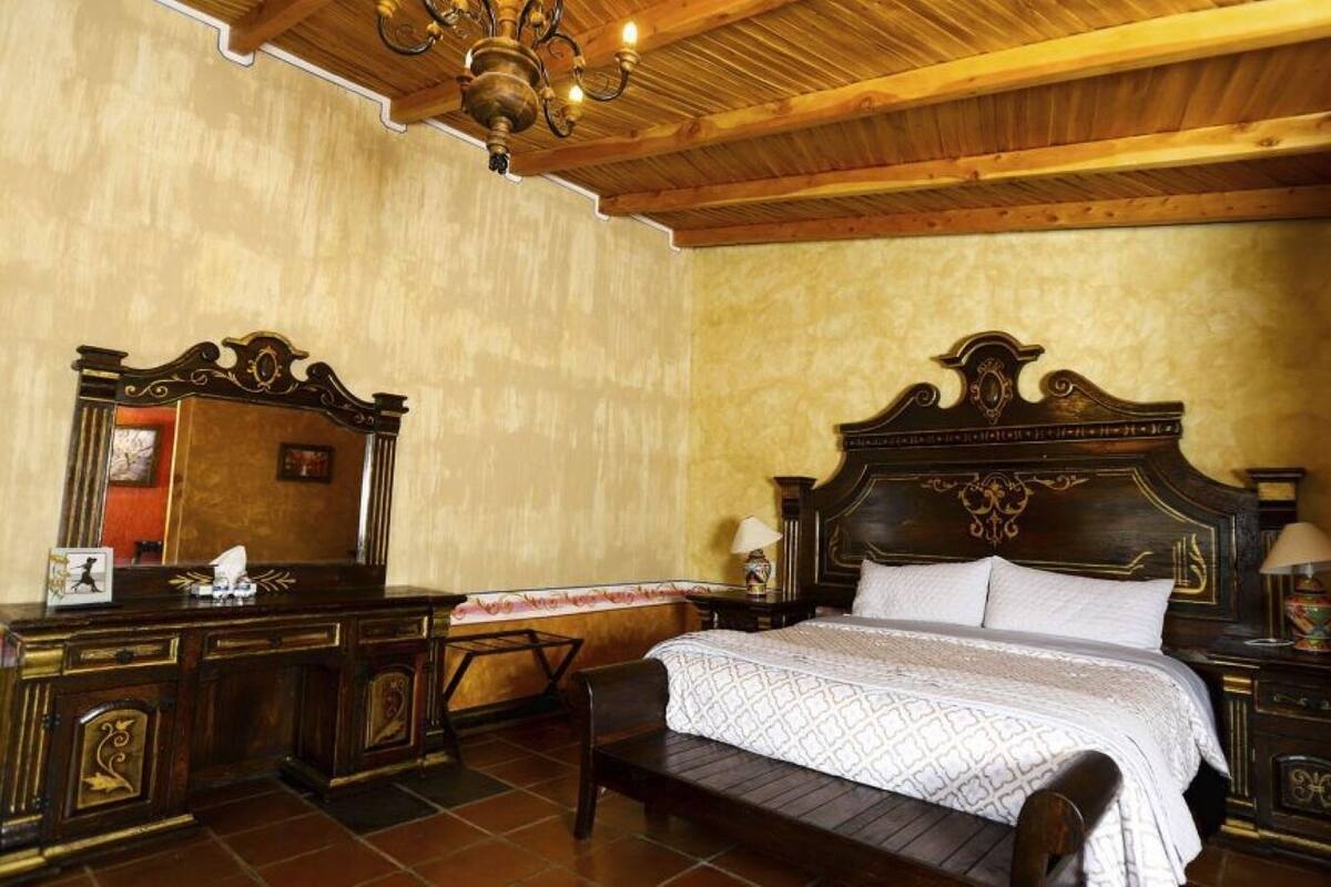 A bedroom with a large bed, wooden headboard, a nightstand, a dresser, a mirror, and a chandelier.