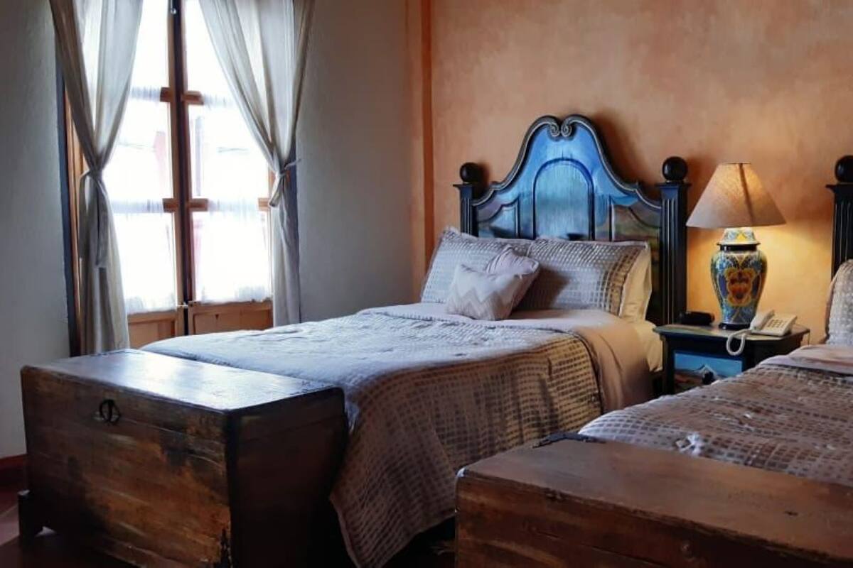A room with two beds, wooden headboards, a nightstand with a lamp, and a large vase.