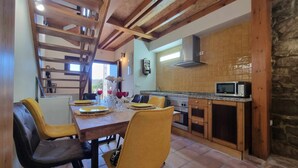 A kitchen with wooden cabinets, a microwave, and a dining area with yellow chairs and a table set for two. - Los Gemelos Vacation Home (San Roque Del Acebal)