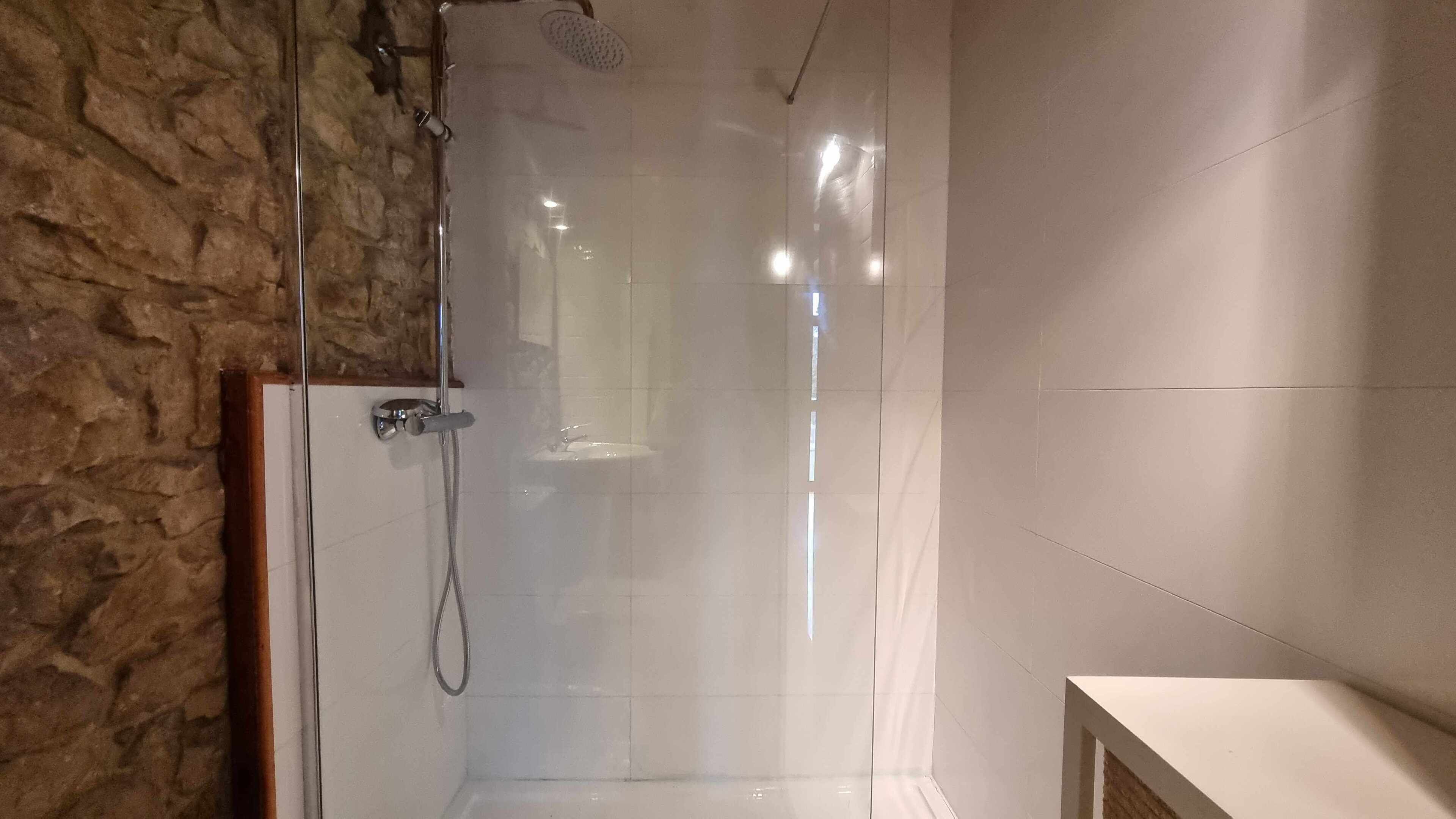 Une salle de bain moderne avec une douche à parois de verre, un mur en pierre et un meuble-lavabo blanc.