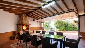 Une terrasse extérieure avec une cheminée en briques, une table à plateau en verre et des chaises en osier.