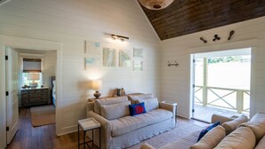 Un salon chaleureux avec un plafond haut, des poutres apparentes, un ensemble de canapés et une vue dégagée sur l’extérieur grâce à une grande porte.