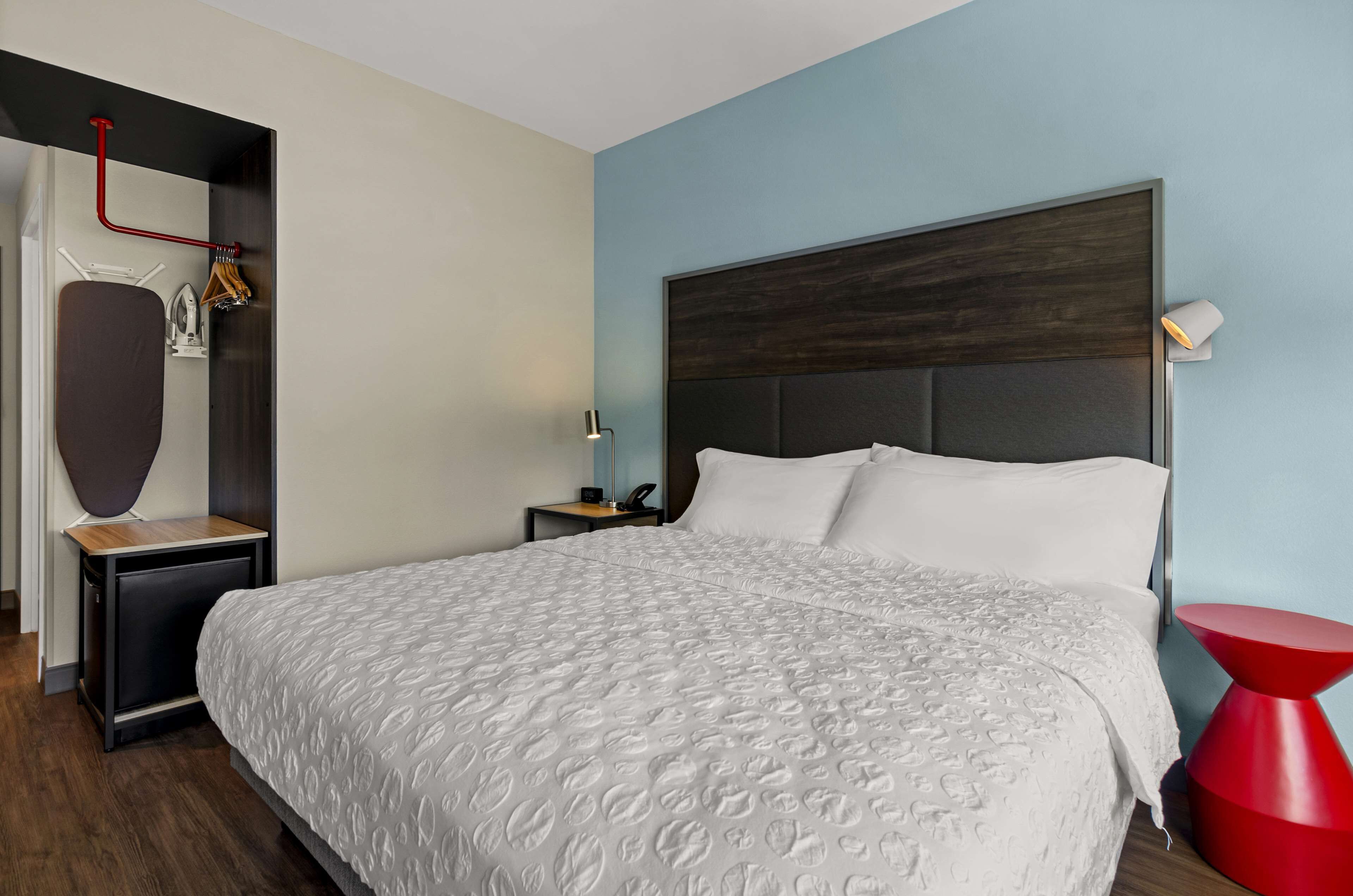 Una habitación de hotel con una cama grande, una mesita de noche, una lámpara roja y un armario.