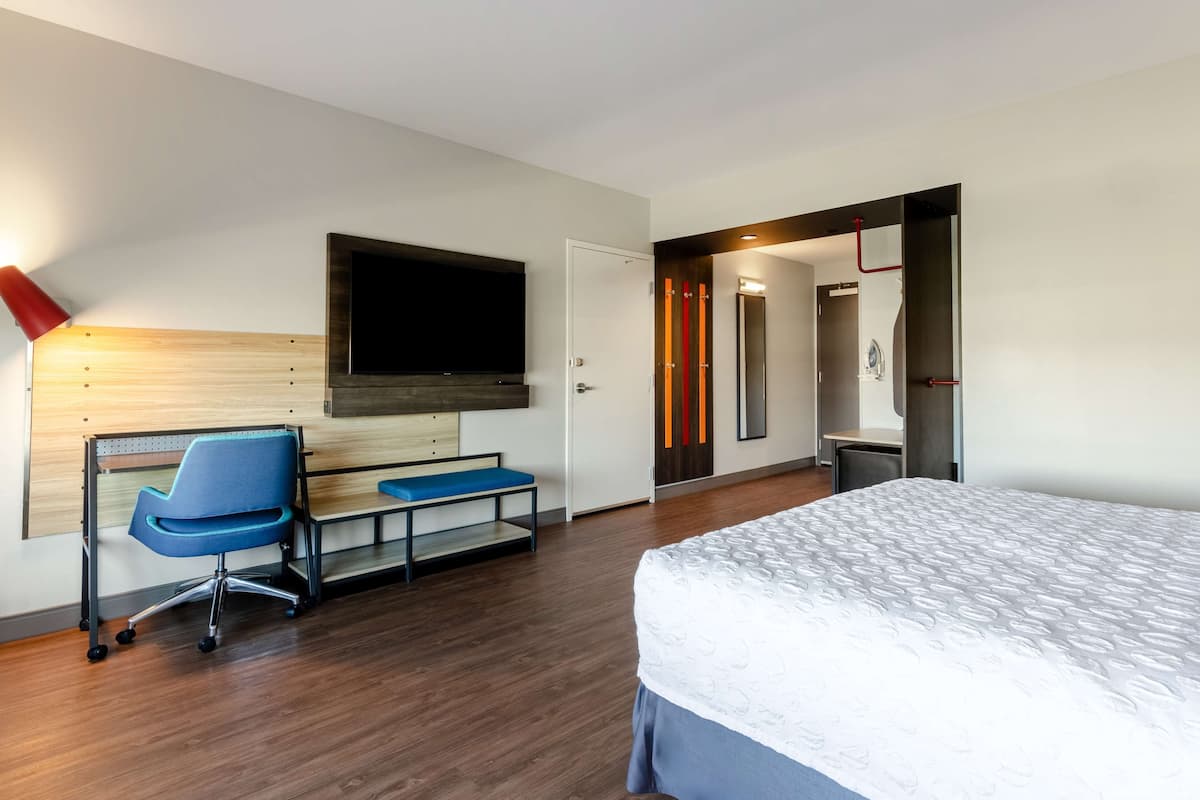 Ein modernes Hotelzimmer mit einem großen Bett, einem Schreibtisch mit Stuhl, einem flachbildfernseher an der Wand und einem Duschbereich.