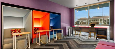 A modern hotel room with a sofa, tables, and chairs, large windows with a view, and a herringbone-patterned carpet.