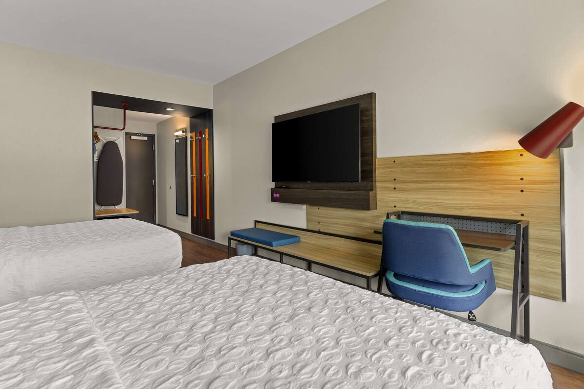 Ein Hotelzimmer mit zwei Betten, einem Wandfernseher, einem Schreibtisch mit Stuhl und einer roten Lampe.