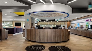A modern hotel reception area with a circular desk, a visible counter, and a 'Top IT' sign in the background. - Tru By Hilton Christiansburg (Christiansburg)