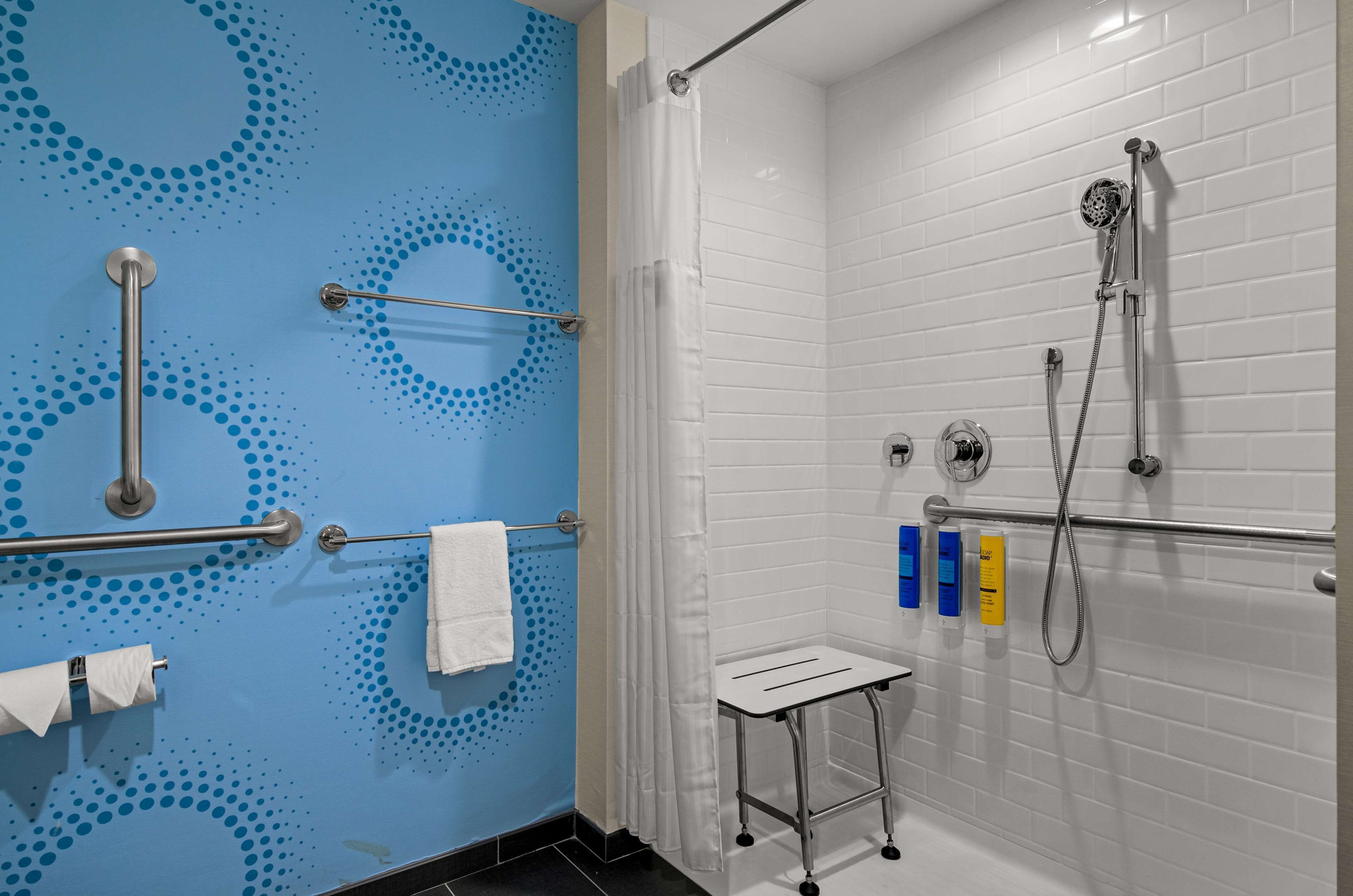 Un baño con pared azul, zona de ducha con azulejos blancos y un toallero blanco.