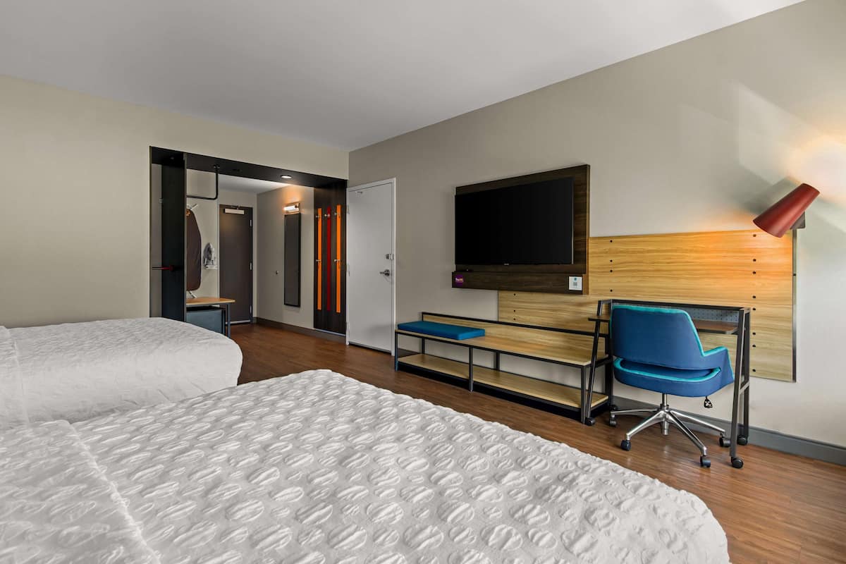 Ein Hotelzimmer mit zwei Betten, einem Schreibtisch mit Stuhl, einem an der Wand befestigten Fernseher und einer roten Lampe.