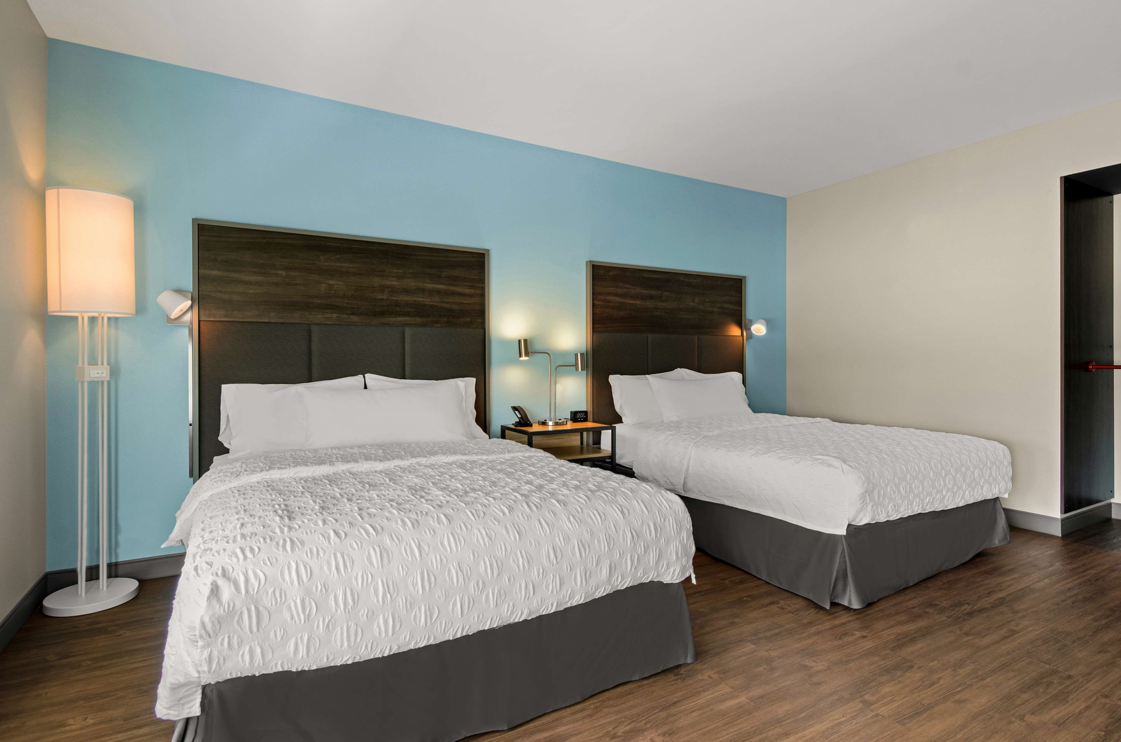 A hotel room with two beds, a nightstand, a lamp, and a door.