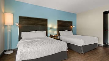 A hotel room with two beds, a nightstand, a lamp, and a door.