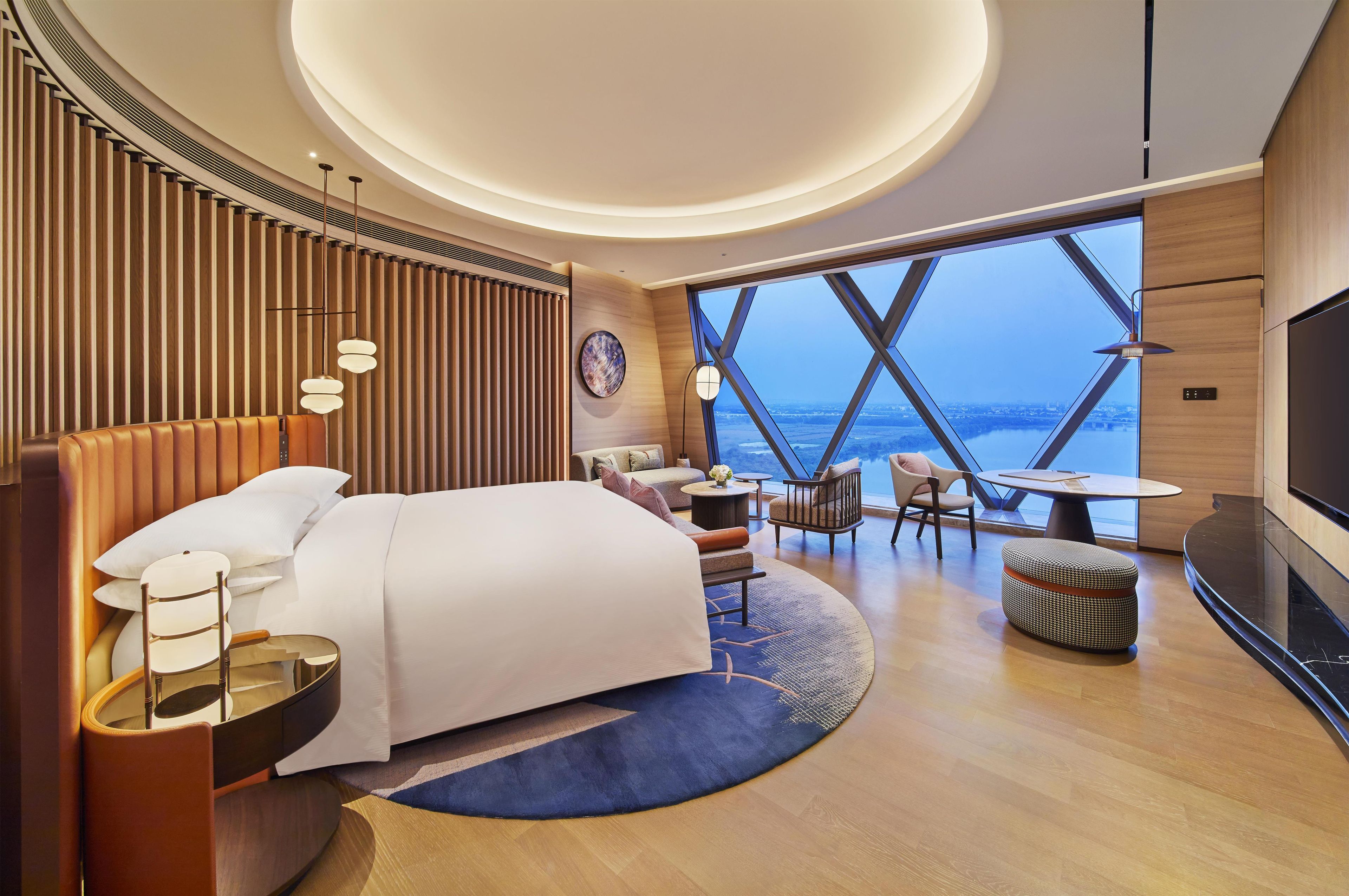 Ein modernes Hotelzimmer mit einem großen Bett, einem Schreibtisch, einem Sessel, einem runden Tisch und einem Fernseher.